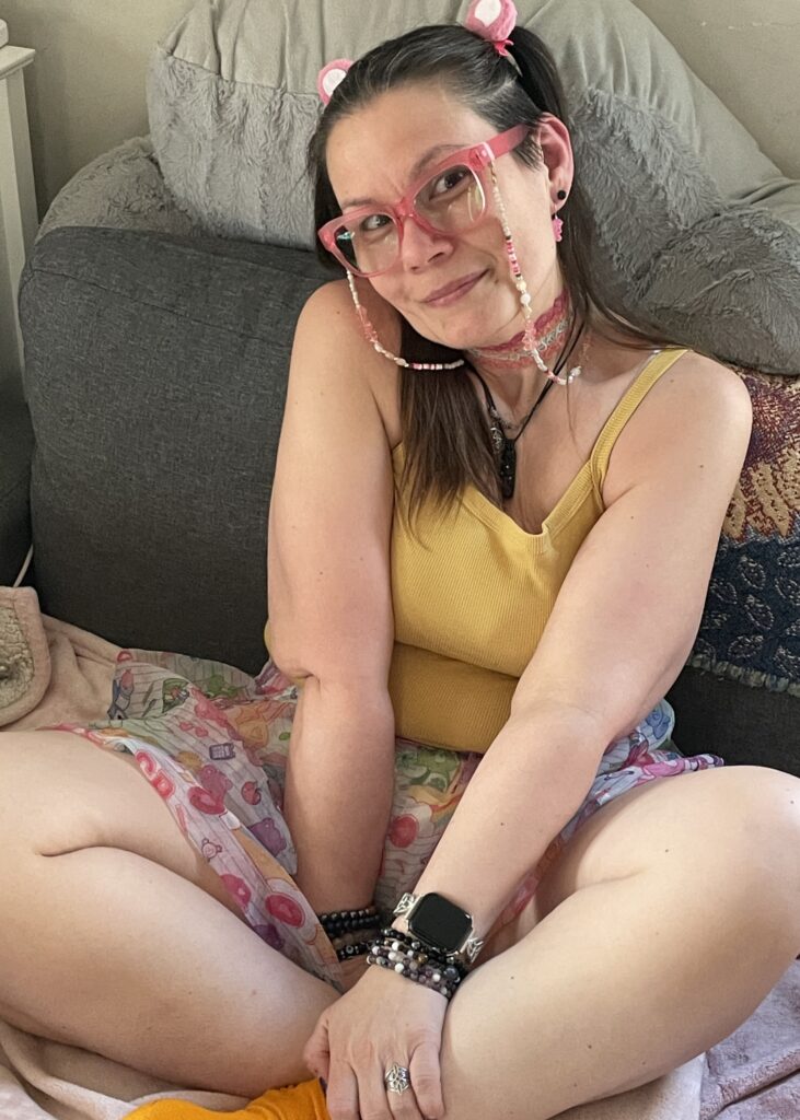 Playful, cozy photo of a whimsical adult embracing a soft, colorful aesthetic with pink glasses and comfy surroundings.